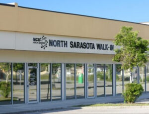 The front of a building. The sign features a logo for MCR Health Services next to text that reads "North Sarasota Walk-In."