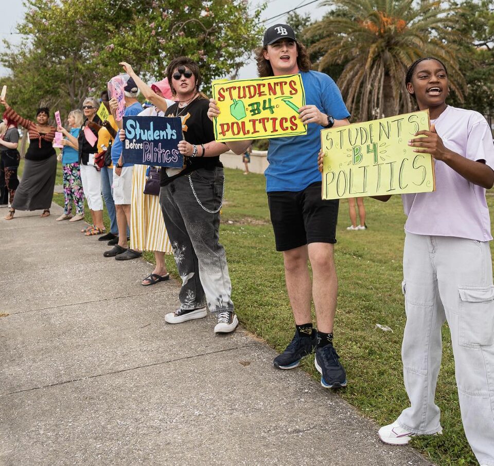 Demonstrators lined up along a sidewalk hold handwritten signs that read "Students before politics."