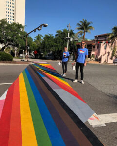 Two people in pride shirts stand next to the downtown Sarasota rainbow crosswalk.