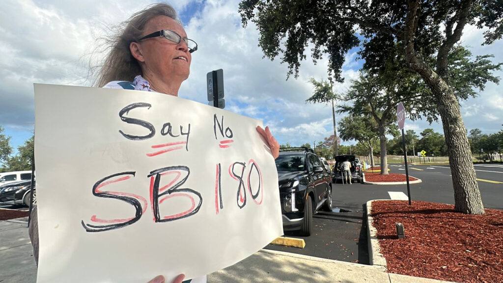 A demonstrator holds a handwritten sign that reads "Say no to SB 180."