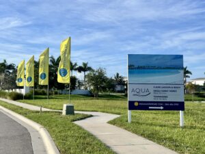 A sign promoting a community called Aqua, which afvertises "4-acre lagoon & beach, single-family homes from the $1m+, and townhomes from the $800".