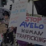 Demonstrators outside in the rain hold signs with messages including "Stop Avelo human trafficking", "Do you really want to fly on the deportation airline for ICE? Boycott Avelo" and "It's a coup; no Trump; No fascist USA".