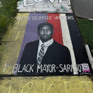 Sidewalk painting of Fredd “Glossie” Atkins with his name written above and "1st Black mayor of Sarasota" written below.