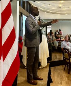 Berny Jacques gesticulates while addressing a crowd in front of a U.S. flag.