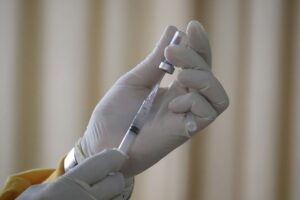 Extreme close-up of someone with gloved hands using a syringe to extract liquid from a tiny container.