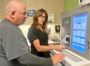 Lisa Gonzalez-Abello. operating an AccuVax machine with assistance.