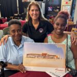 Helen Neal-Ali, Geri Chaffee, and Shinece Davis presenting a printed rendering of the Newtown Family Center building and smiling.