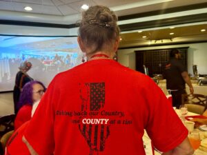 Photo of the back of someone's red t-shirt which reads "Taking back our Country, one COUNTY at a time".