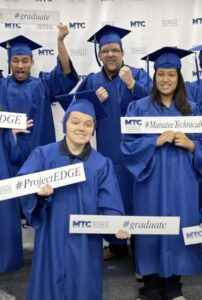 Graduates in blue caps and gowns holding MTCD-branded signs with hashtags like #ProjectEDGE, #graduate, and #ManateeTechnicalCollege.