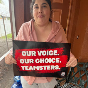 Outside the front door of their home, a person holds a sign that reads "Our voice. Our choice. Teamsters."
