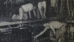 Grainy black and white photo of stagehands working behind the scenes on a stage production.
