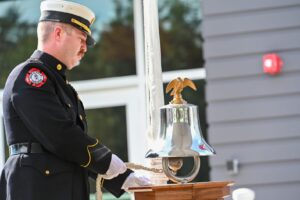 A firefighters in a ceremonial uniform rings a bell.