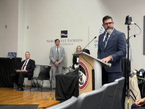 Anastasios Kamoutsas speaking at a podium at Northwest Florida State College.