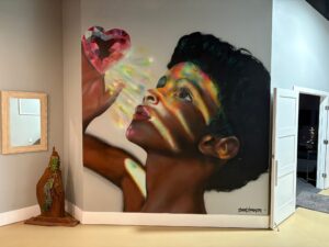 Mural on an interior wall of a young Greg Cruz reaching up toward a heart-shaped crystal which casts colorful stripes of bright light across his face.