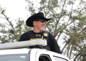 Rick Wells smiling, peeking through the sunroof of a police vehicle.