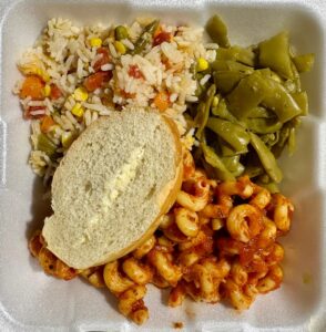 A styrofoam tray of food including rice, pasta, snow peas, and buttered bread.