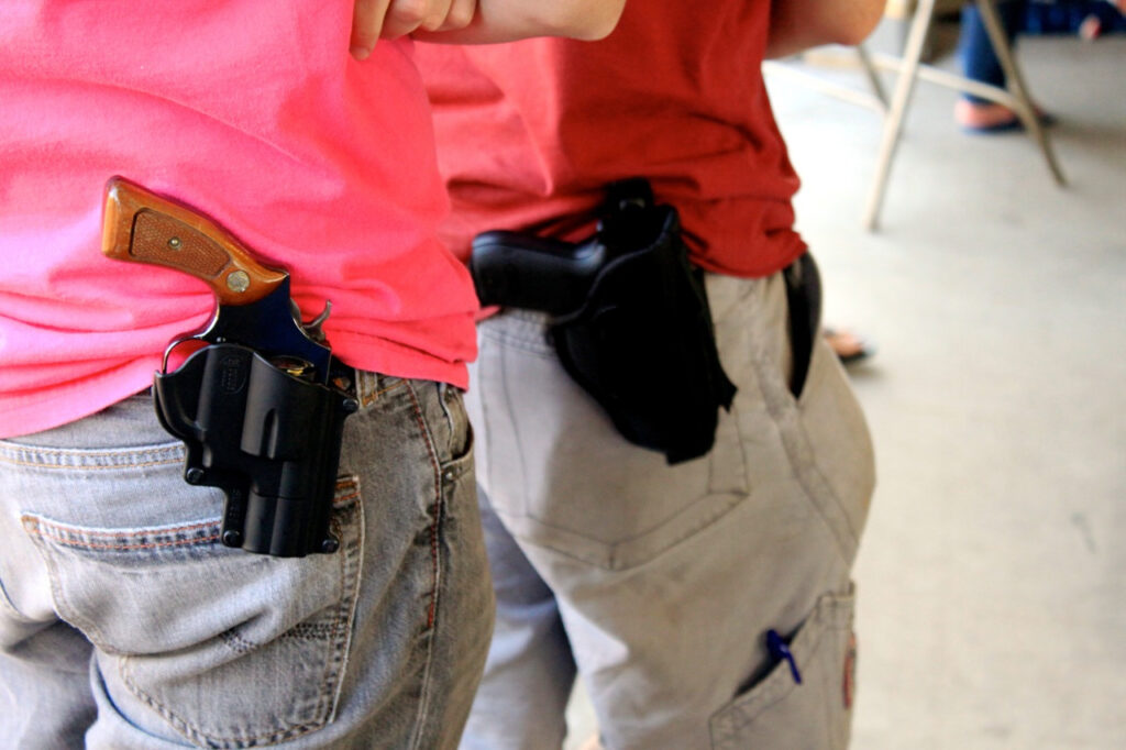 Close-up of two people's holstered handguns.