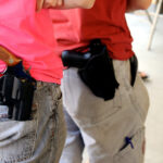 Close-up of two people's holstered handguns.