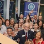 Photo of a crowd of people smiling in front of a Sister Cities Association of Sarasota banner.