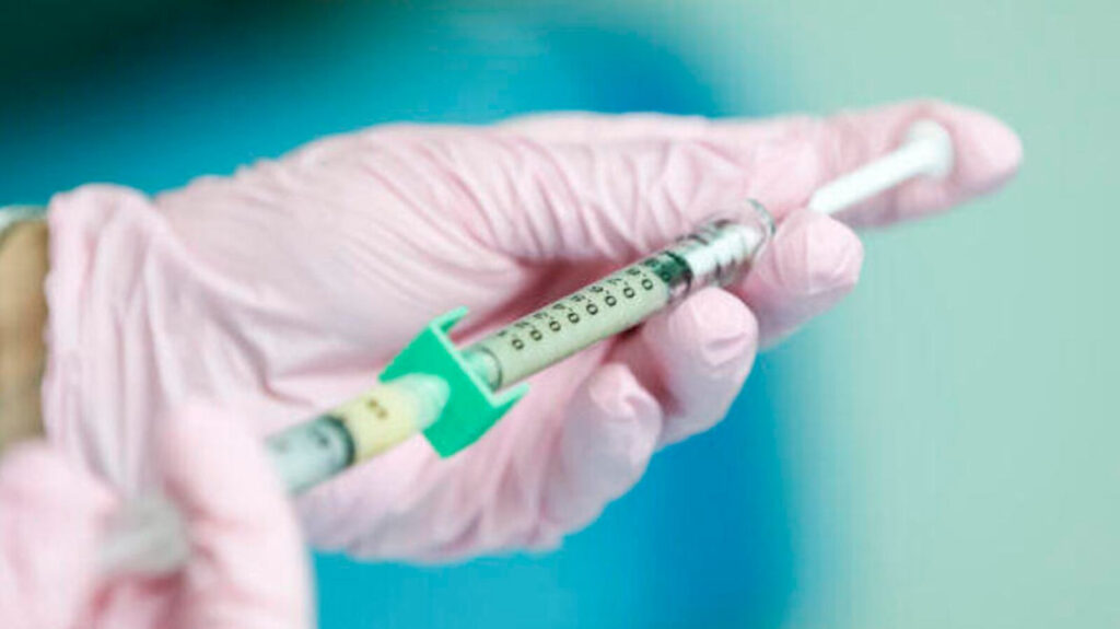 Photo of gloved hands holding a syringe.