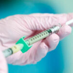 Photo of gloved hands holding a syringe.