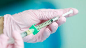 Photo of gloved hands holding a syringe.