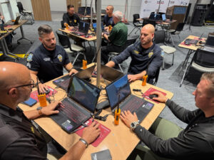 Police officers sit around tables using laptops.