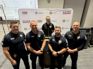 Police officers smile and pose in front of a backdrop with Texas A&M, FEMA, ALERRT, and NCIER logos.