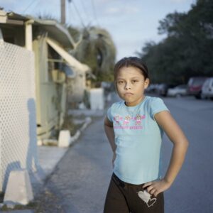 Photo of a young girl on a neighborhood road facing the viewer.