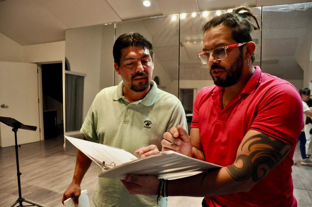 Carlos Ramírez and Edward Ossa stand and look at documents in a binder together.
