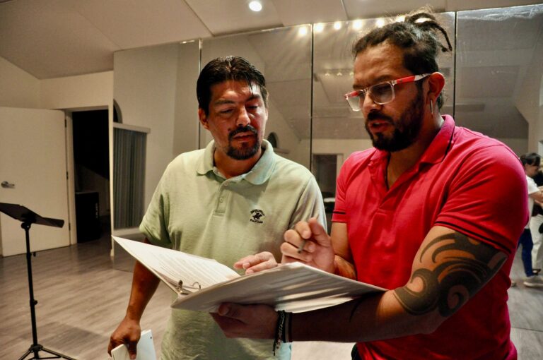 Carlos Ramírez and Edward Ossa stand and look at documents in a binder together.