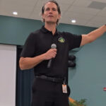 Terry Conner gesticulating while speaking into a microphone in a school cafeteria.