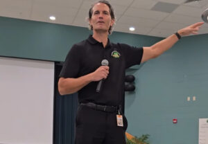 Terry Conner gesticulating while speaking into a microphone in a school cafeteria.