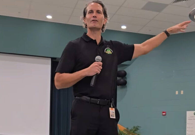 Terry Conner gesticulating while speaking into a microphone in a school cafeteria.