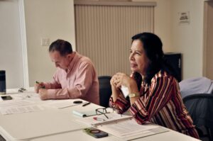 Juan Pablo Salas and Elvira Sánchez-Blake sit together at a table. Salas takes notes while Sánchez-Blake speaks.