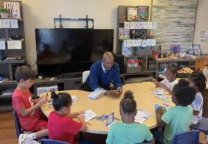 Jimmy Glover seated at a table with six young children in an elementary school classroom.
