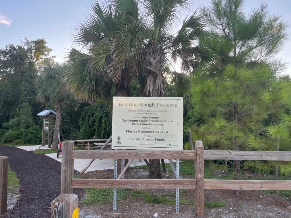 A sign in a park that reads:Red Bug Slough Preserve Funding for the acquisition of this site was provided by Sarasota County Environmentally Sensitive Lands Protection Program and the Florida Communities Trust using Florida Forever Funds