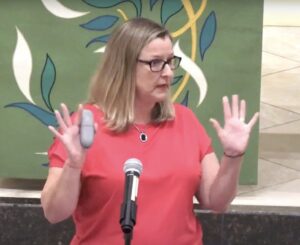 Jeanne Zokovich Paben gesticulating while speaking in front of a microphone.