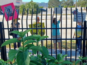 Demonstrators behind a fence. One holds a sign that reads "Trump is a bad egg".