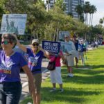 Demonstrators near downtown Sarasota wear shirts and hold signs that read "Unite & rise! Defend democracy LWV SRW" and "Uphold our Constitution and the rule of law".