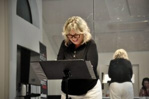 Marie Angée laughs while reading from a binder resting on a stand.