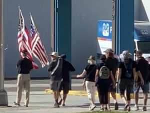 A group of demonstrators walks together, the leaders holding American flags.