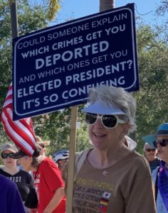 A demonstrator in a crowd holding a sign that reads "Could someone explain which crimes get you diported and which ones get you elected president? It's so confusing".