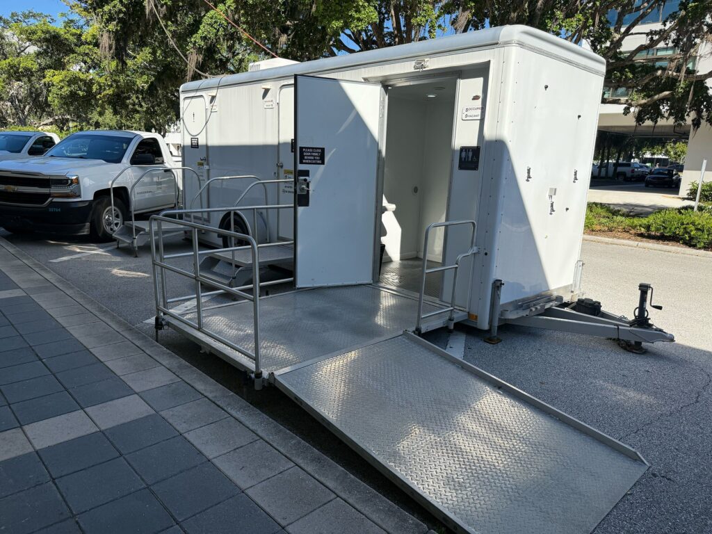A compact restroom trailer with a metal access ramp leading up to the entrance.