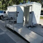 A compact restroom trailer with a metal access ramp leading up to the entrance.