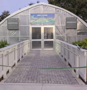 A greenhouse tent with a banner over the entrance that reads "Welcome to the Extension Educational Outreach Garden Greenhouse".
