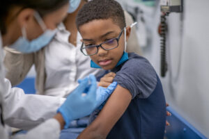 A masked healthcare provider administers a vaccine to a child.