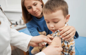A child is comforted by an adult as a healthcare professional gives the child a vaccine.