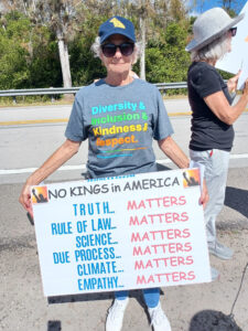 A demonstrator wearing a wearing a shirt that reads "Diversity & Inclusion & Kindness & Respect" holds a sign that reads: No kings in America Truth... matters Rule of law... matters Science... matters Due process... matters Climate... matters Empathy... matters
