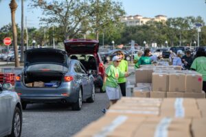 Workers distributing boxes to a line of cars.